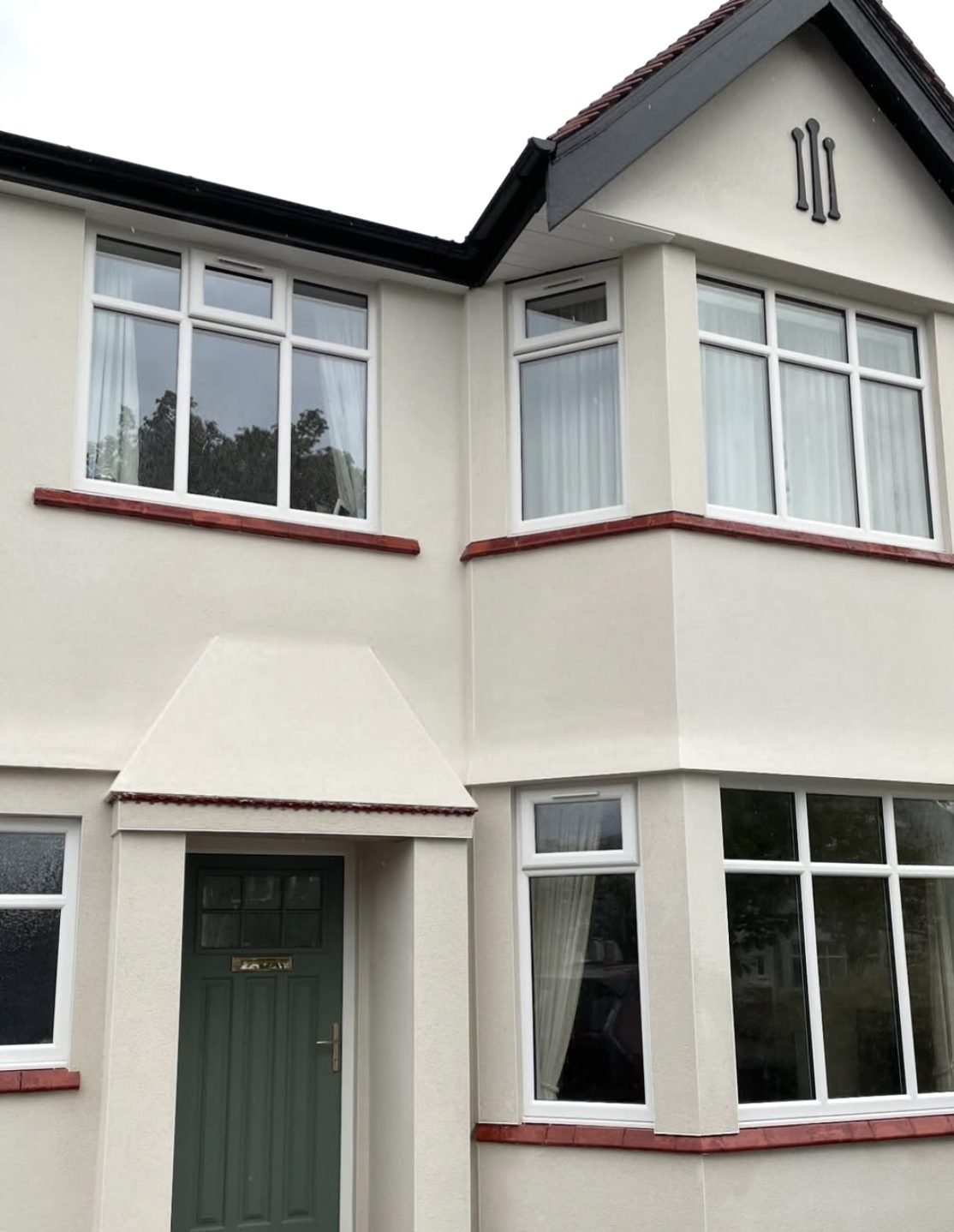 1930s semi-detached house with curved bay windows in cream render and red tile sills