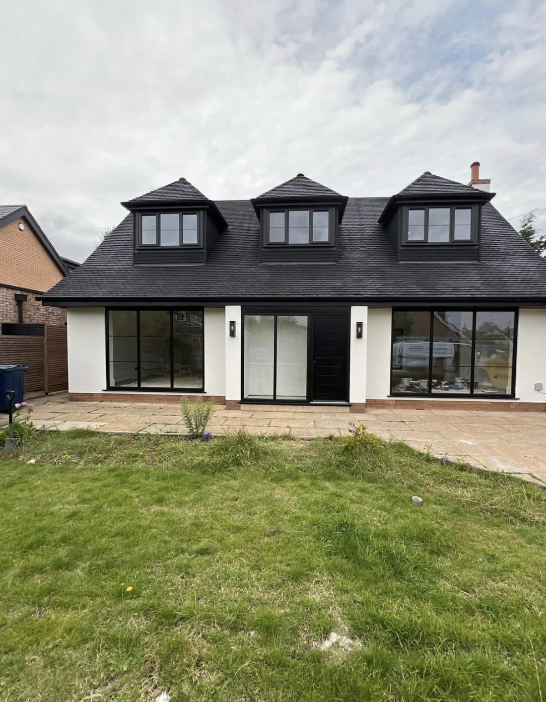 Back of a chalet-style house in white render with three dark dormers and wide glazing