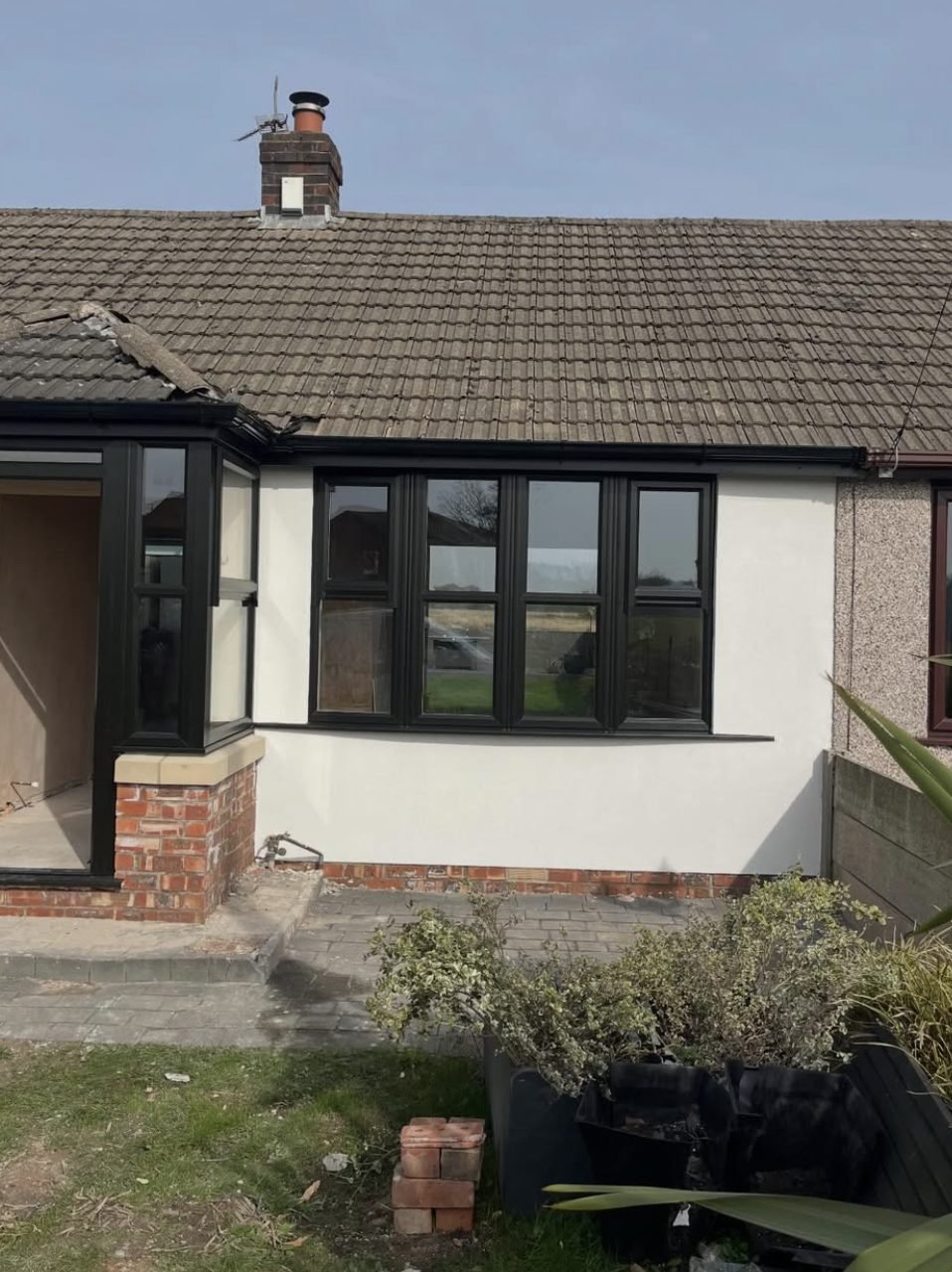 Bungalow with smooth white render beside a neighbouring wall still in pebbledash
