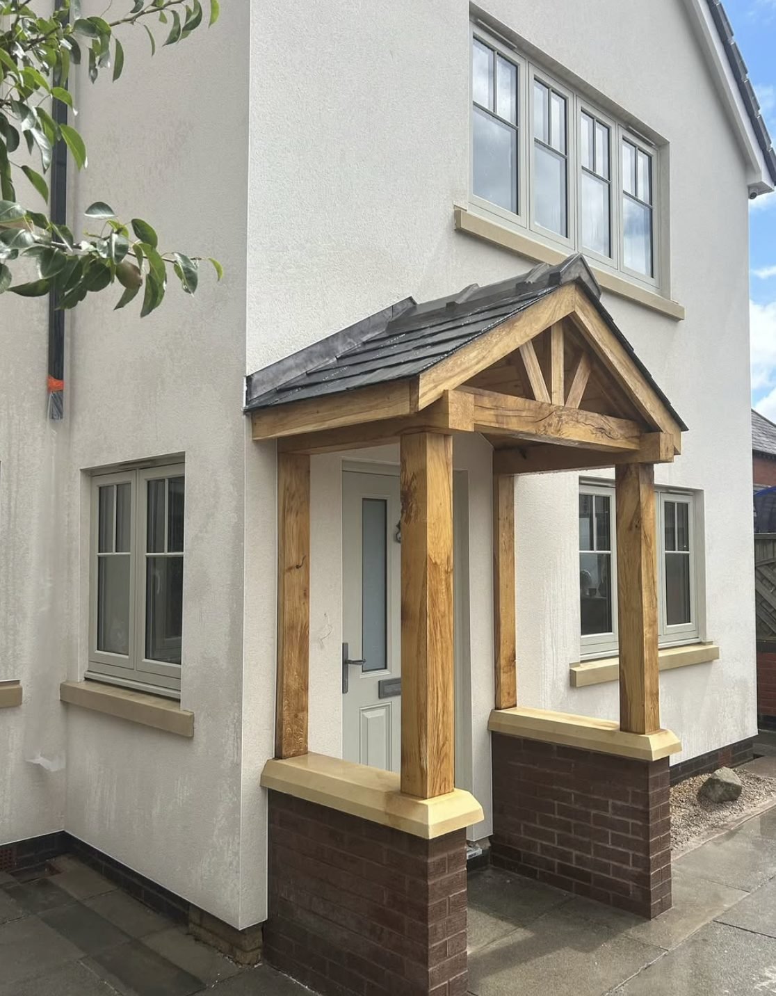 Cream rendered house front with a timber porch on brick piers