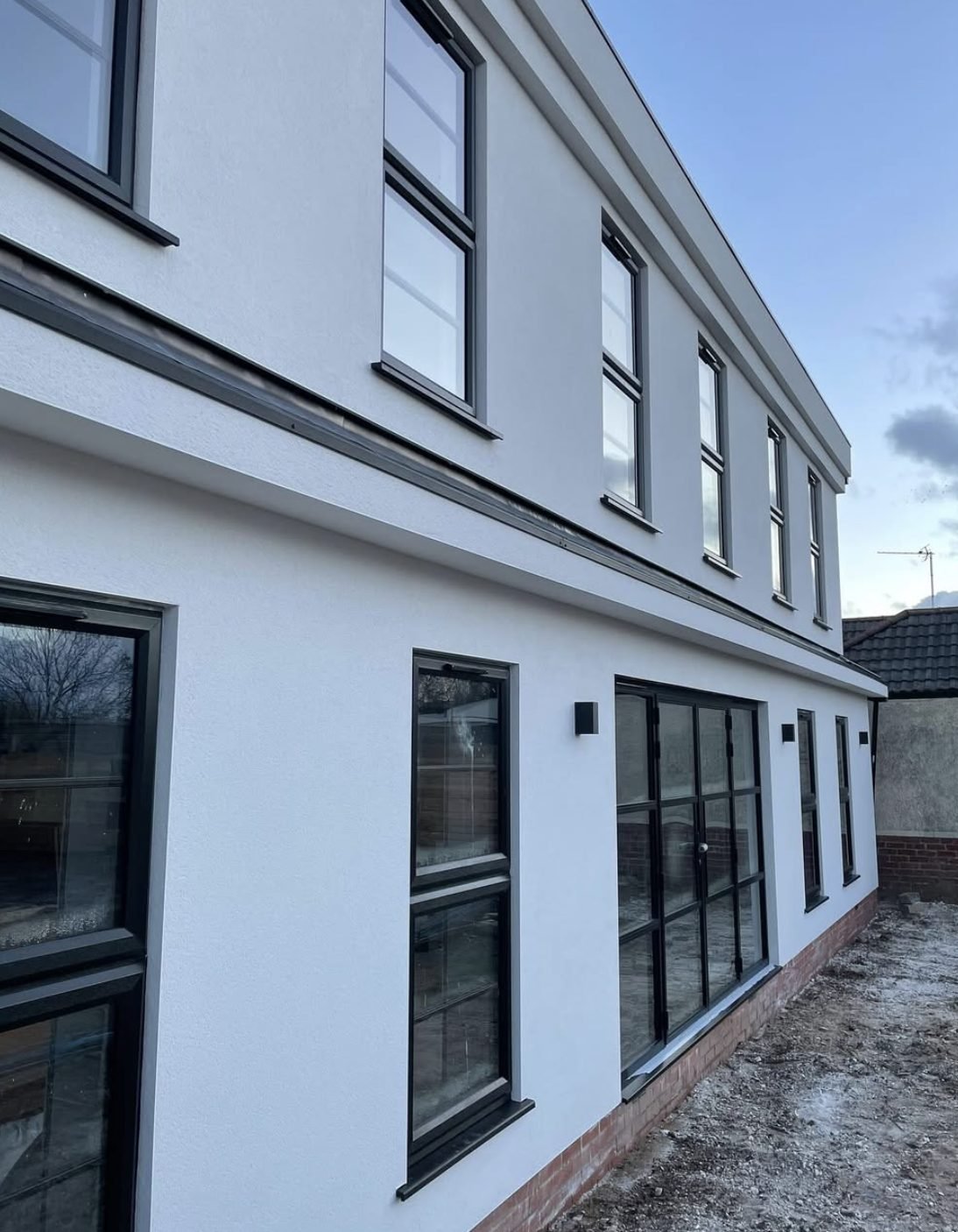 Long two-storey side wall in smooth white render with a dark band and black windows