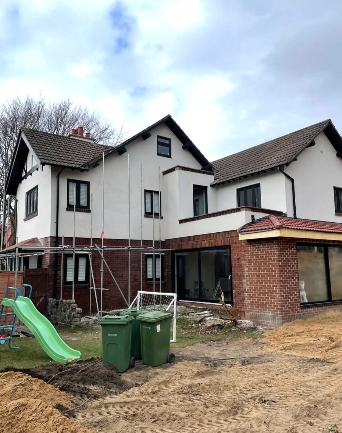 Back of a large house with the upper floor rendered and scaffold over a brick extension