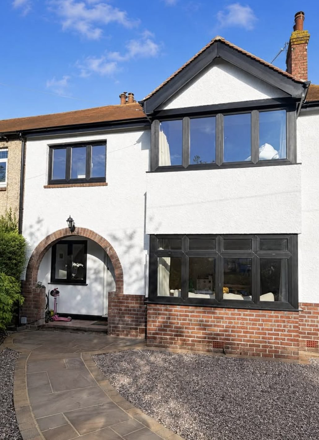 Terraced house in white render with a gabled bay and a red brick arch over the porch