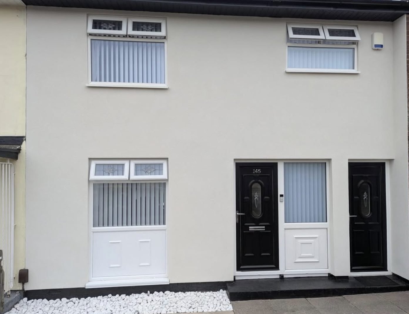 Two terraced house fronts in matching smooth cream render with black doors