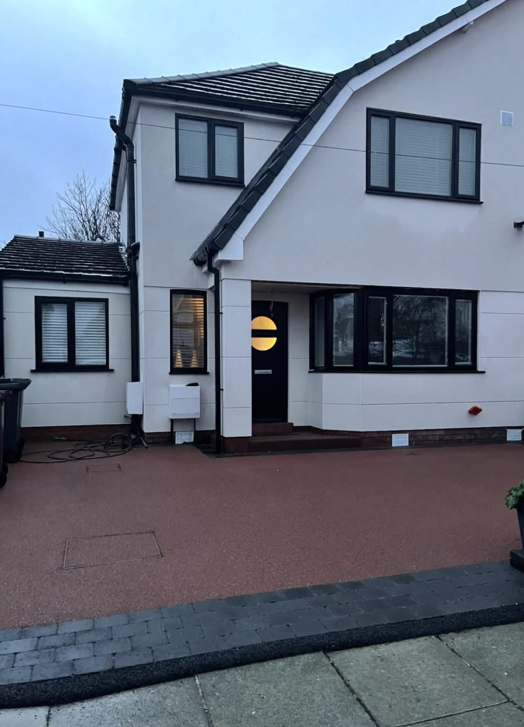 House in white render with dark grey window frames and a red paved drive